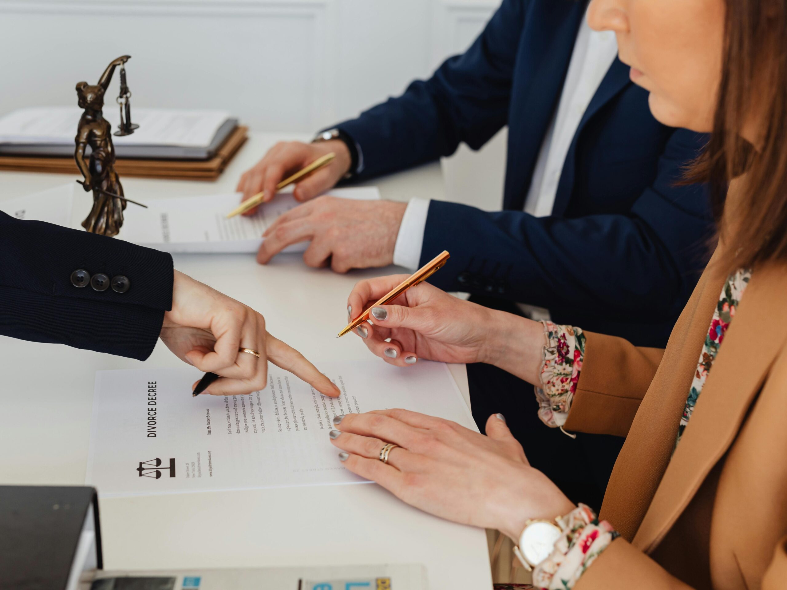 Hands signing a divorce decree, with a justice statue nearby, symbolizing legal proceedings.